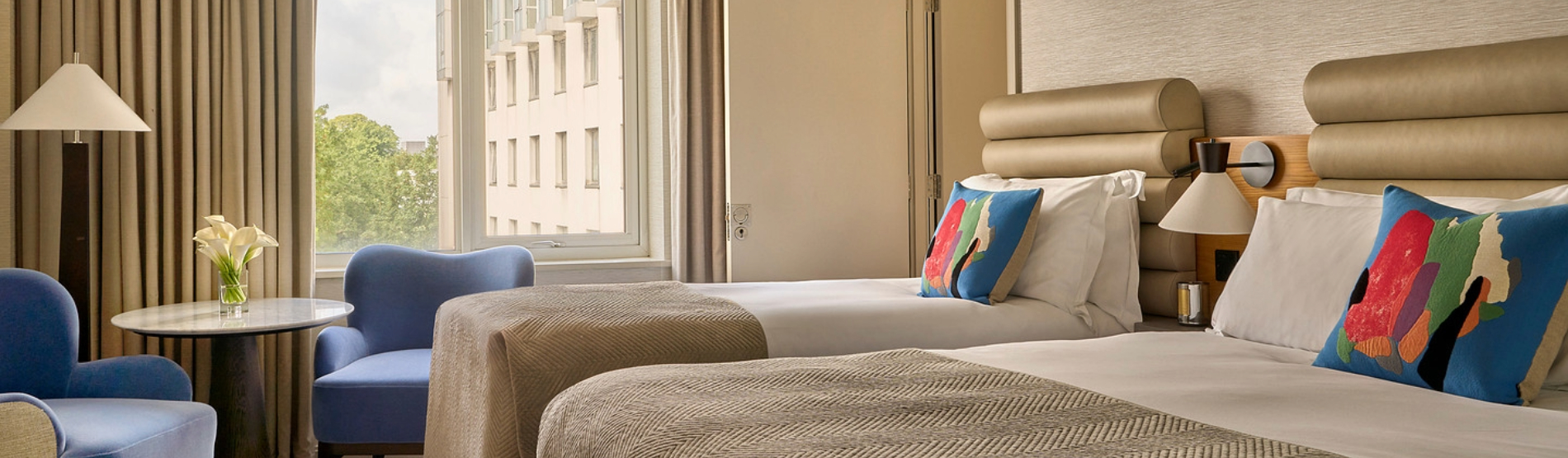 A Classic Room at The River Lee Hotel, Cork, showing a double bed and a single bed, with two blue armchairs positioned in front of the window.