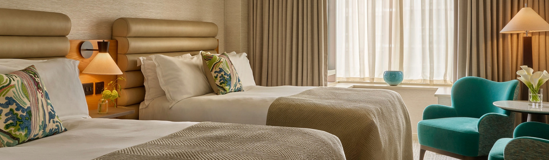 Classic Room at The River Lee, Cork, features two double beds, a stylish lamp, and a cozy seating area with two turquoise armchairs and a small coffee table placed in front of a large window