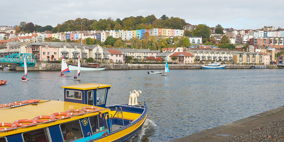 A vibrant yellow and blue ferry boat gliding across Bristol's floating harbour, viewed from the waterfront.