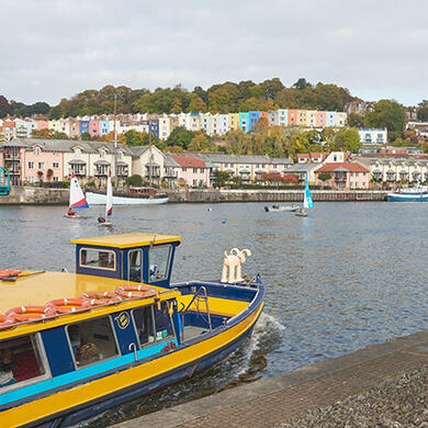 A vibrant yellow and blue ferry boat gliding across Bristol's floating harbour, viewed from the waterfront.