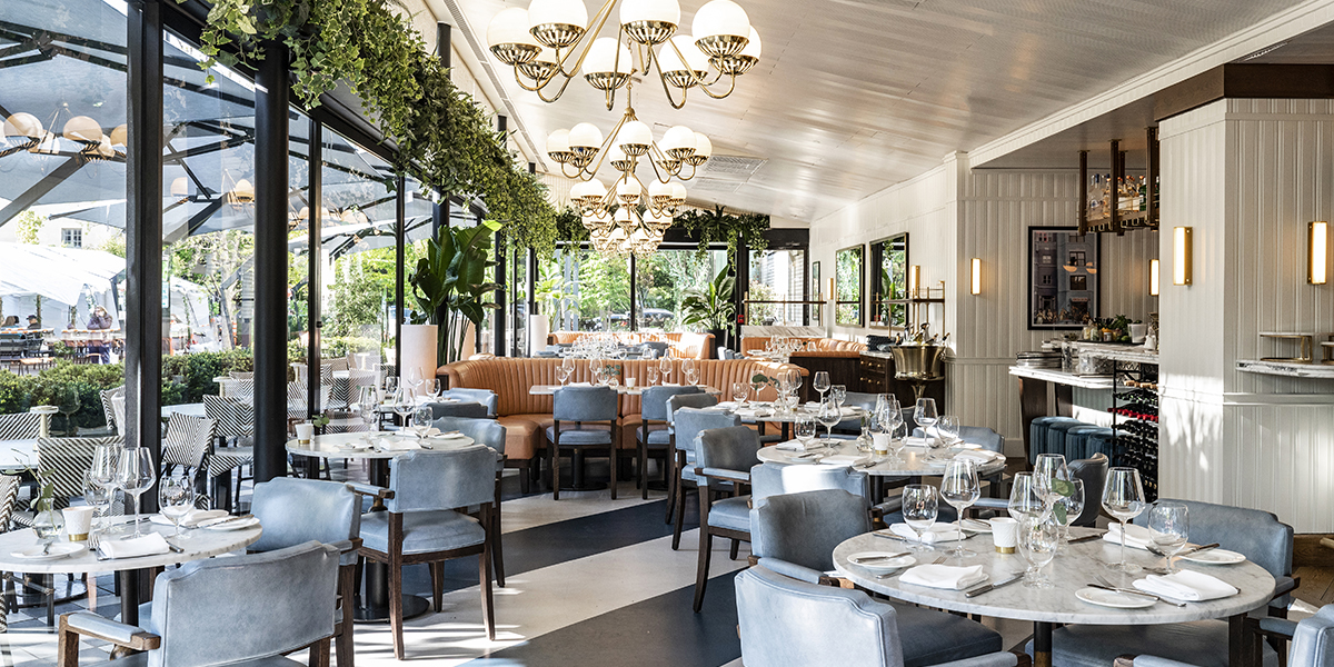 The Pembroke restaurant in Washington, D.C., featuring marble tables set for dinner alongside vibrant orange banquette seating.