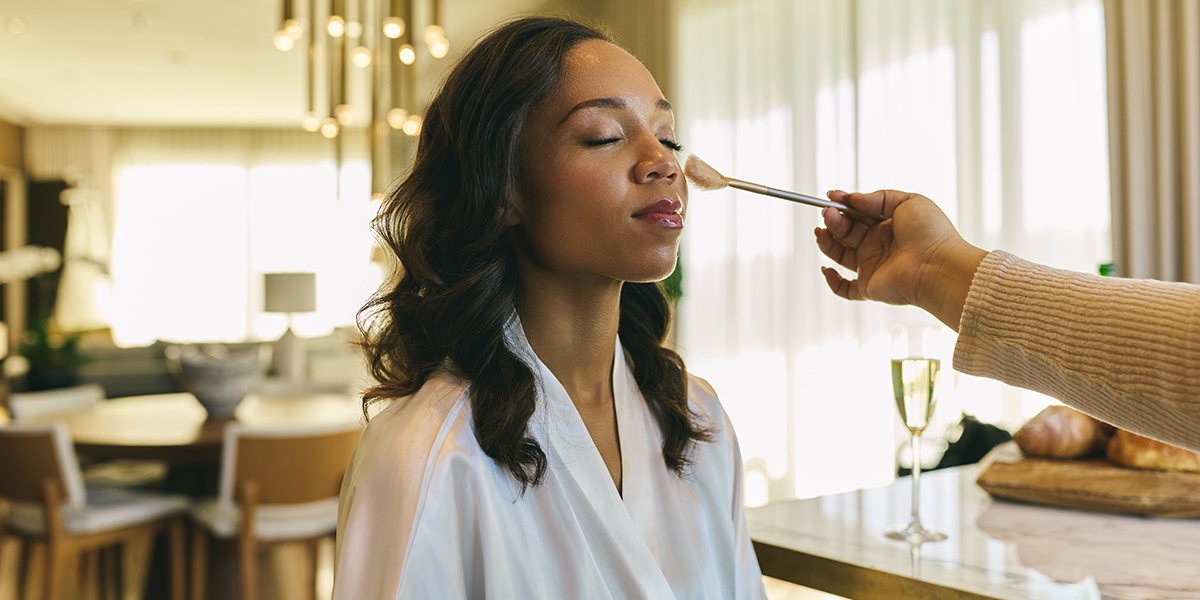 Morning-of wedding preparations in a luxury suite at The Dupont Circle, featuring a bride relaxed in her robe with champagne and professional makeup styling.