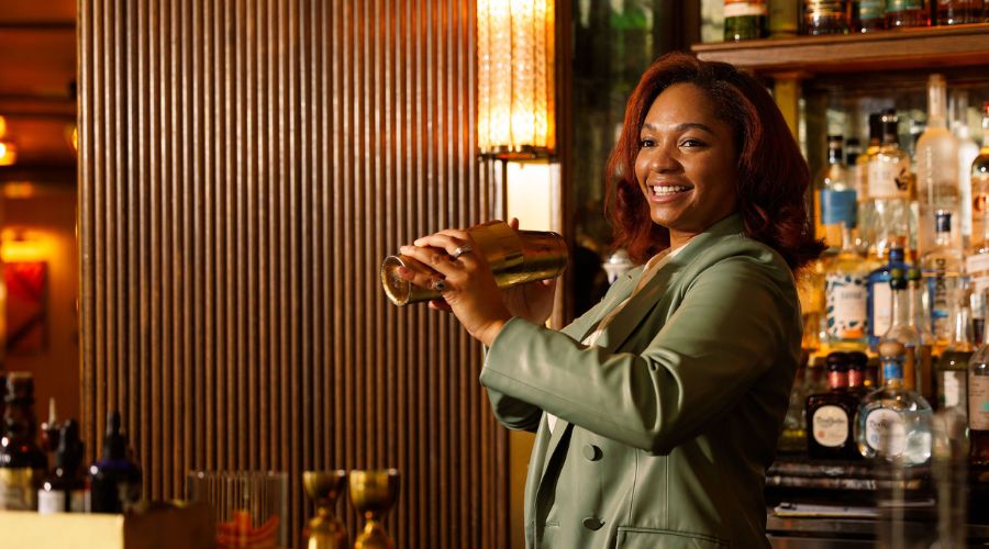 A smiling female bartender shaking a cocktail behind the counter at Doyle Bar