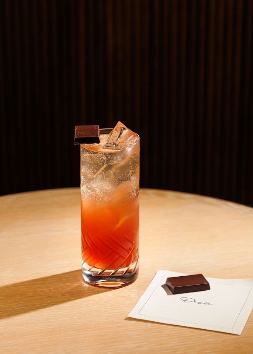 The GoGo Swing bourbon and prosecco cocktail in a tall glass with a chocolate garnish next to the Doyle Bar menu.