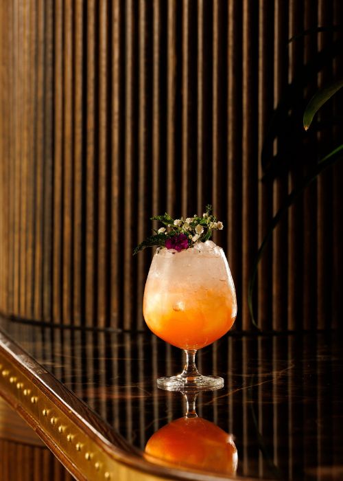 The Silent Spring non-alcoholic cocktail at Doyle Bar, an orange botanical drink served with ice in a stemmed goblet glass and garnished with fresh flowers
