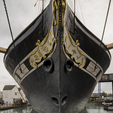 The magnificent SS Great Britain, a black iron hulled ship with elegant golden detailing, docked in Bristol Harbour under a clear sky. Its historic presence dominates the waterfront