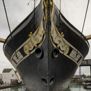 The magnificent SS Great Britain, a black iron hulled ship with elegant golden detailing, docked in Bristol Harbour under a clear sky. Its historic presence dominates the waterfront