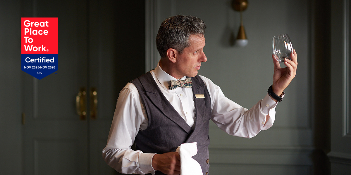 A close-up of a bartender ensuring a glass is spotless, symbolizing attention to detail, alongside the "Great Place to Work UK" recognition badge earned by The Doyle Collection teams.