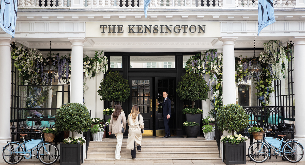 Two women entering The Kensington Hotel as a concierge opens the door, exterior view of the building representing The Doyle Collection’s hospitality.