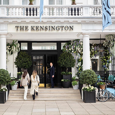 Two women entering The Kensington Hotel as a concierge opens the door, exterior view of the building representing The Doyle Collection’s hospitality.