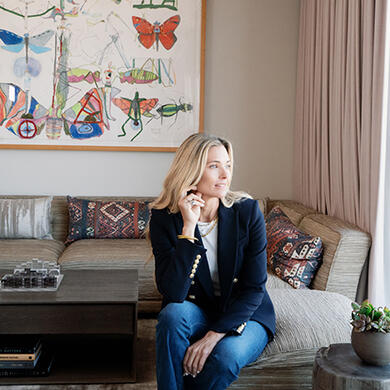 Veronica Beard, dressed in a navy blazer, stands in a suite at The Dupont Circle Hotel, looking out the window