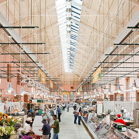 Shoppers admiring colorful flower arrangements and fresh food displays at the indoor Eastern Market, capturing the lively community atmosphere of a weekend market day.