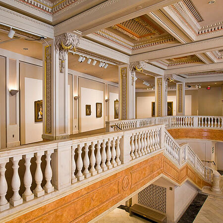 The bright, newly renovated Great Hall of the National Museum of Women in the Arts, featuring a grand white marble double staircase, classical columns, and an airy, sunlit hallway.