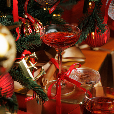 A detailed shot of a champagne coupe, crafted from Waterford crystal for a partnership with The Kensington and The Bloomsbury Hotel. The glass is filled with rose champagne and is placed next to festive Christmas decorations other crystal pieces.