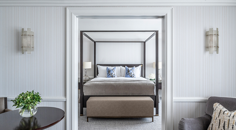 A luxurious four-poster bed in a bright, elegant suite bedroom at The Westbury Hotel, ideal for a solo traveler.