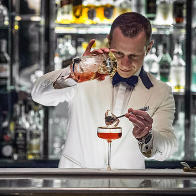A bartender carefully crafts cocktails behind the sleek bar at Sidecar.