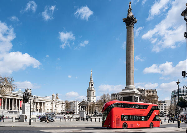 A red bus drives through Trafalgar Sqaure in London