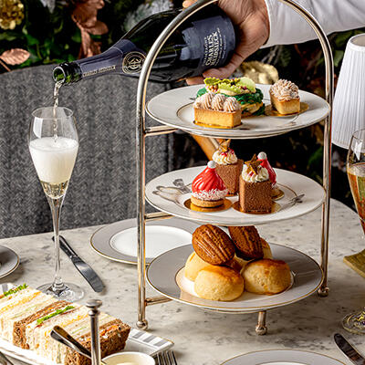 Indulgent Afternoon Tea at The Bloomsbury Hotel, featuring a three-tiered stand of delicious bites, as a waiter pours champagne into a flute glass.