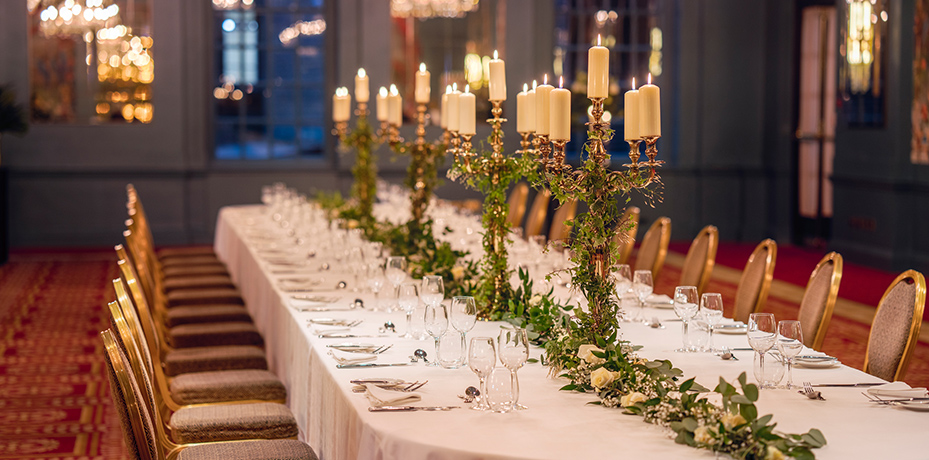 A private event setup in the George V Hall at The Bloomsbury, showcasing a candlelit long table with exquisite flower arrangements and sophisticated decor
