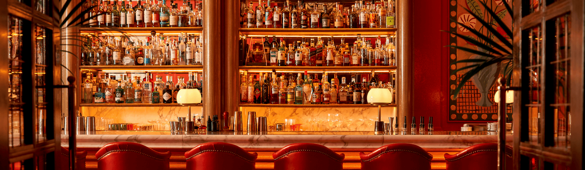 View into The Coral Room from the doorway, focusing on the marble bar stocked with drinks and surrounded by elegant bar chairs, highlighting the vibrant and glamorous interior