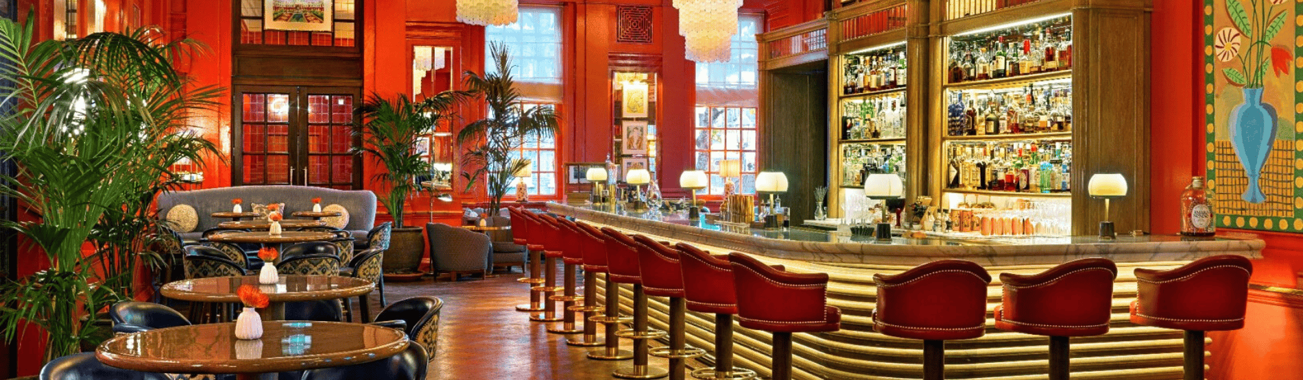 The Coral Room at the Bloomsbury Hotel with vivid coral walls, Murano chandeliers, and a sweeping marble bar, set up for a stylish reception in a bright, elegant space.