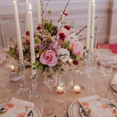 A close-up of a wedding table set with white roses, greenery, elegant dinnerware, and various candles at The Bloomsbury hotel