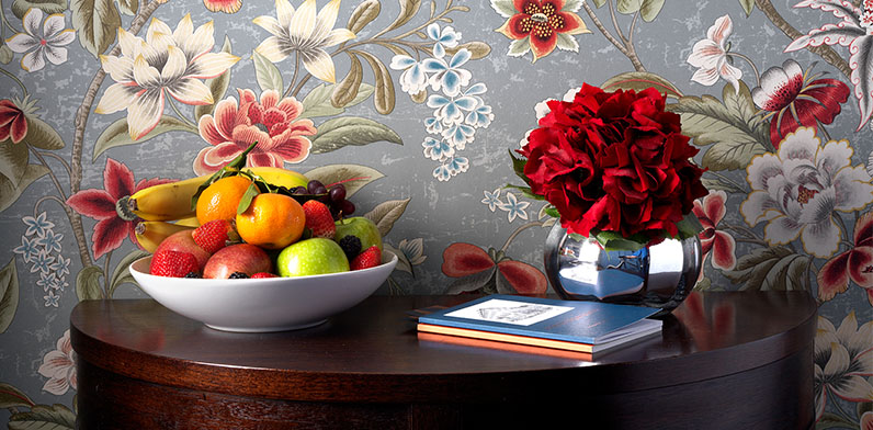 A fruit bowl and vase of red flowers on a wood table