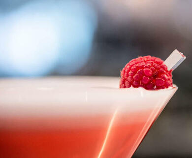 A pink cocktail in a martini glass with a raspberry garnish