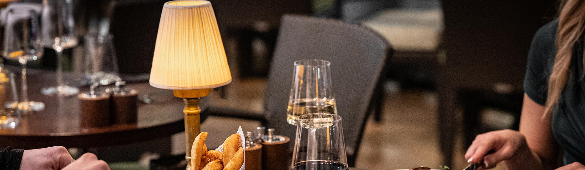 Elegant dining at Ricks Restaurant in The Bristol Hotel. Two guests savoring their steak and fish main courses, complete with wine pairings.