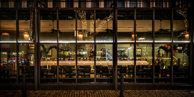 Evxterior view of River Grille restaurant at The Bristol hotel, seen through the large windows. The dimly lit space is empty, with tables and chairs neatly arranged for dinner, and warm light creating a romantic atmosphere.