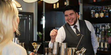 A bartender at The Bristol hotel's bar, Rick's, smiles while preparing to serve a customer.