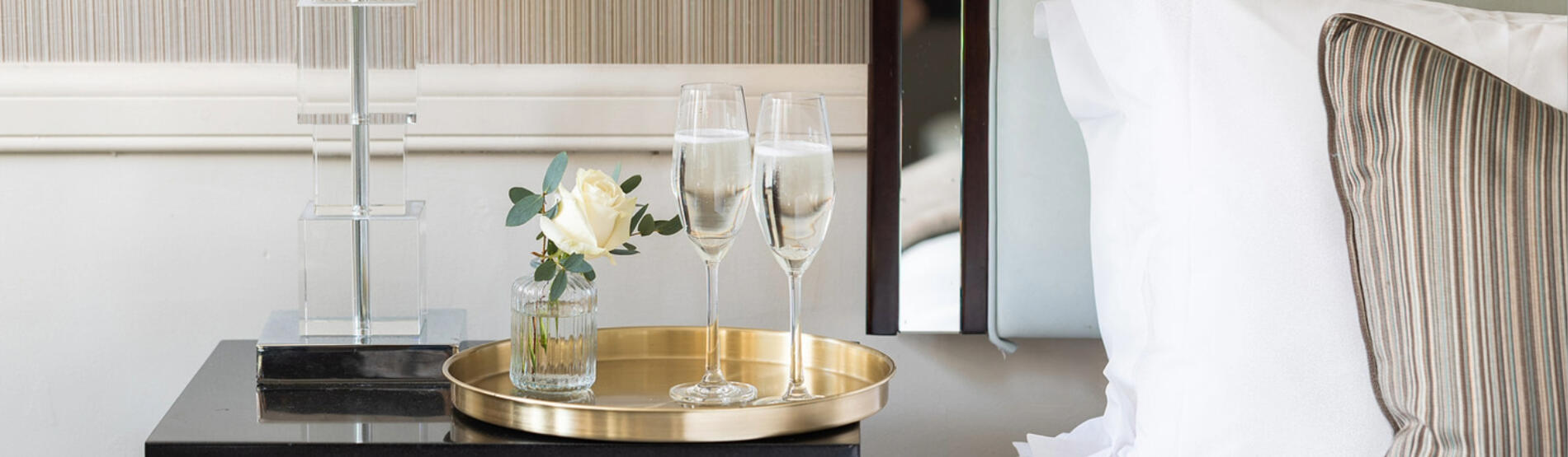 Guest room at The Bristol Hotel featuring a bed with a white rose and two glasses of champagne for the Summer Escape package.
