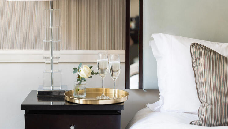 Guest room at The Bristol Hotel featuring a bed with a white rose and two glasses of champagne for the Summer Escape package.