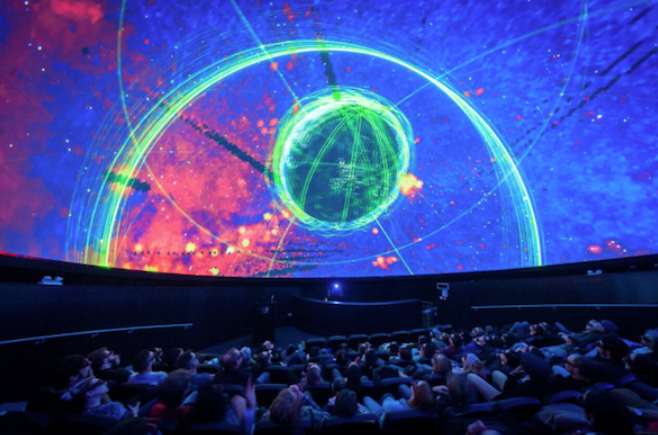 Visitors seated in a planetarium at We The Curious, a science centre in Bristol. The ceiling displays a projection of planets, creating an immersive experience