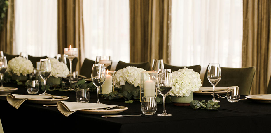 Long table set up for wedding with black table cloth, white flowers and white candles