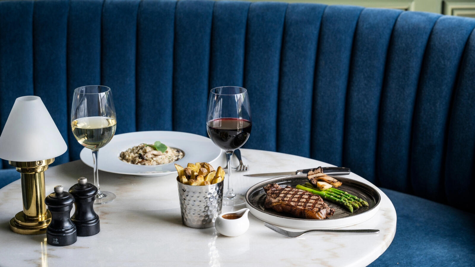 Dinner is on a table at the Hawthorn Restaurant inside The Croke Park Hotel, featuring a pasta dish with a white wine pairing and a steak with asparagus paired with a red wine