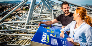 A couple smiling joyfully on the Croke Park Skyline Tour, with a stunning panoramic view of Dublin city sprawling below them.