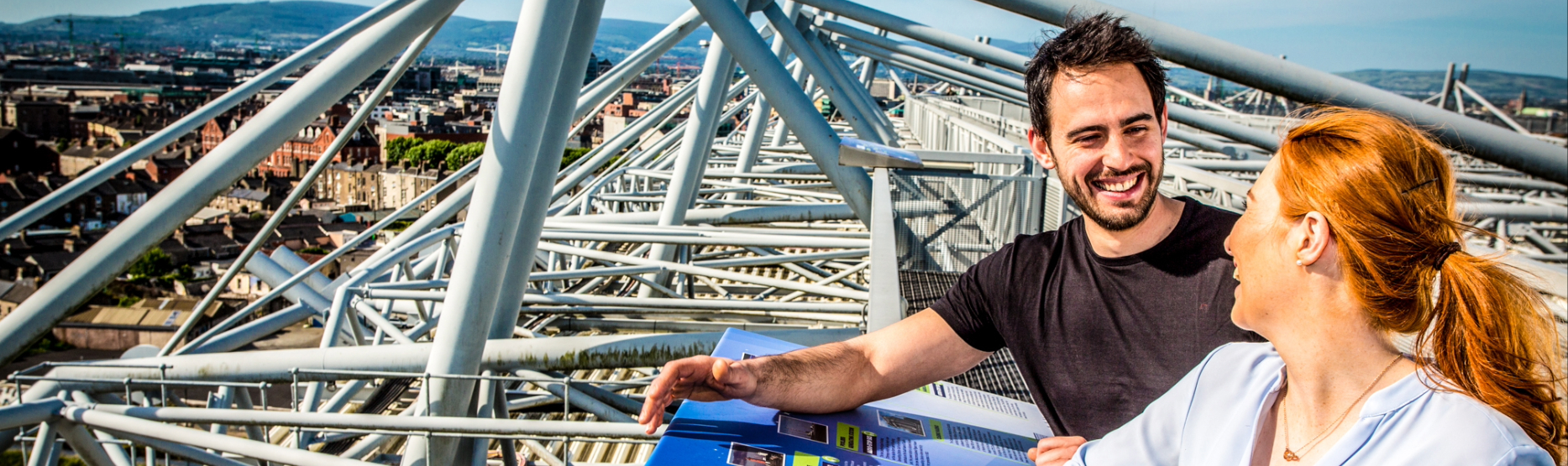 A couple smiling joyfully on the Croke Park Skyline Tour, with a stunning panoramic view of Dublin city sprawling below them.