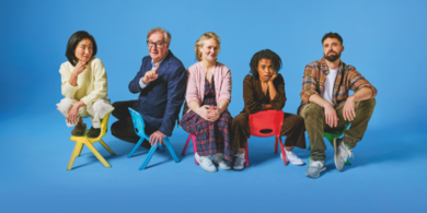 Cast members of the Gate Theatre’s production of Eureka Day sitting in small, colorful children's chairs against a vibrant blue background. The actors are posed in various expressions, capturing the play's comedic atmosphere.