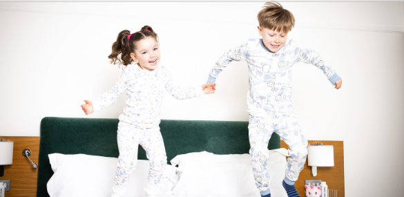 Family fun at The Croke Park hotel where two happy children are jumping on a bed in a spacious hotel room.
