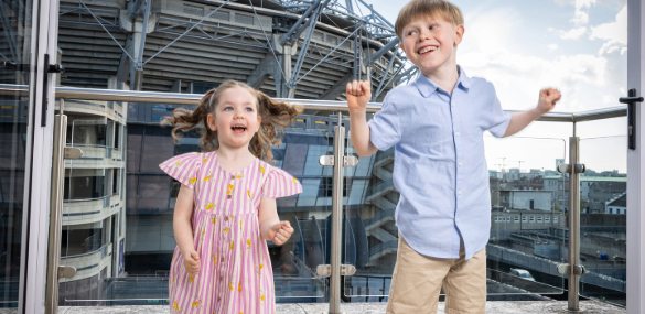 Kids celebrating their family GAA stay at The Croke Park Hotel, joyfully jumping on their room's balcony with a clear view of Croke Park Stadium.