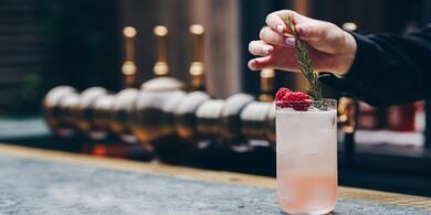 Cocktail being garnished with fresh raspberries and a sprig of rosemary