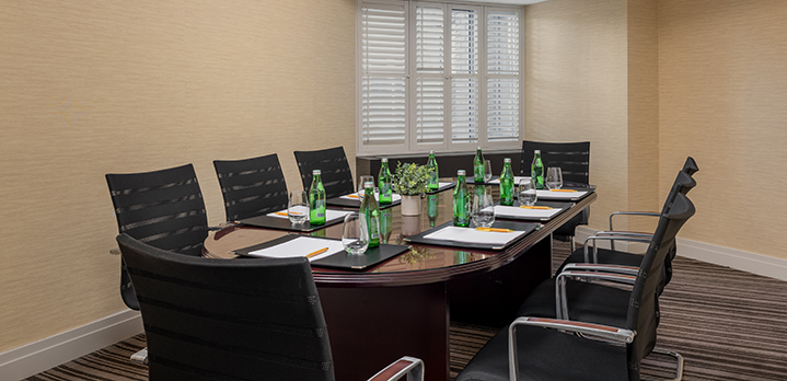 Bboardroom setup in the Douglass Room featuring a rectangular table and seating for eight. The organized tabletop, complete with meeting essentials and a fresh floral centerpiece