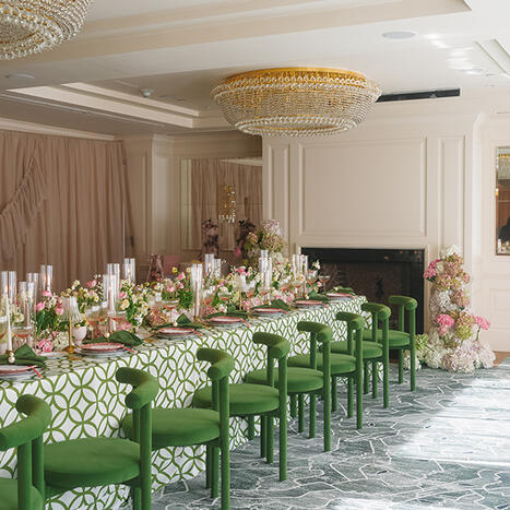 An elegant social event in the Foxhall room featuring a long banquet table decorated with lush pink and green floral arrangements. Bright green chairs complement the coordinated table decor, creating a cohesive and stunning garden-inspired atmosphere.