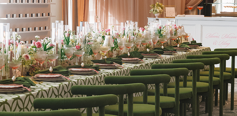 A beautifully styled long table set for a celebration in the Foxhall room, adorned with ornate pink flowers and green accents. The striking green chairs add a bold pop of color to the sophisticated pink-and-green event design.