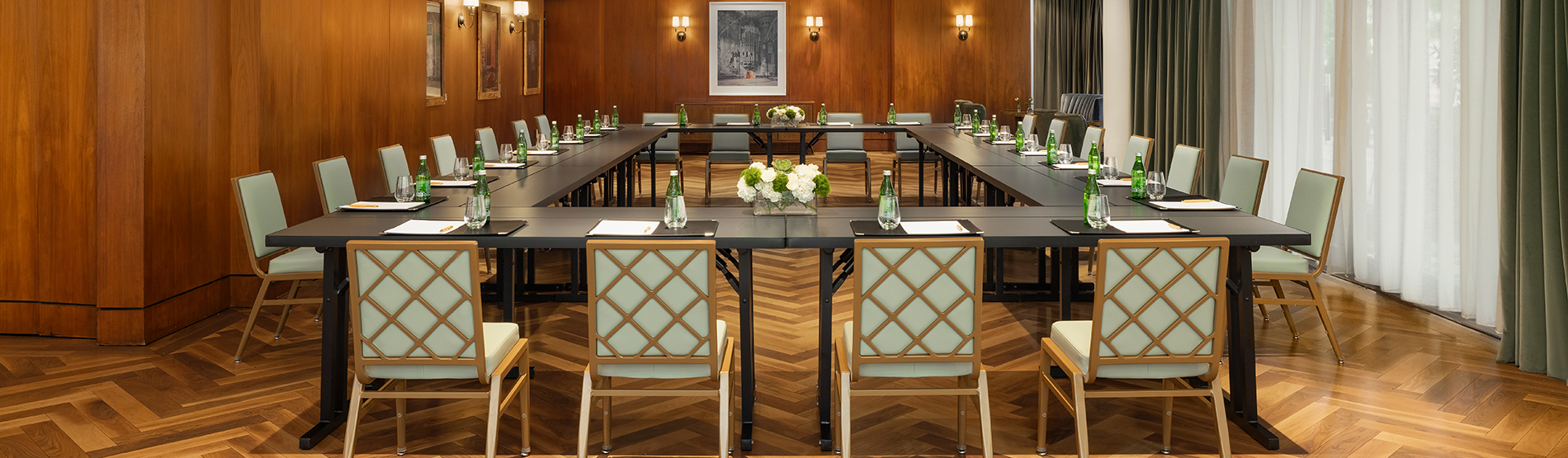 The Glover Park event space set in a hollow square configuration. Large windows fill the room with natural light, highlighting the symmetrical table arrangement and the professional, airy atmosphere of the meeting.