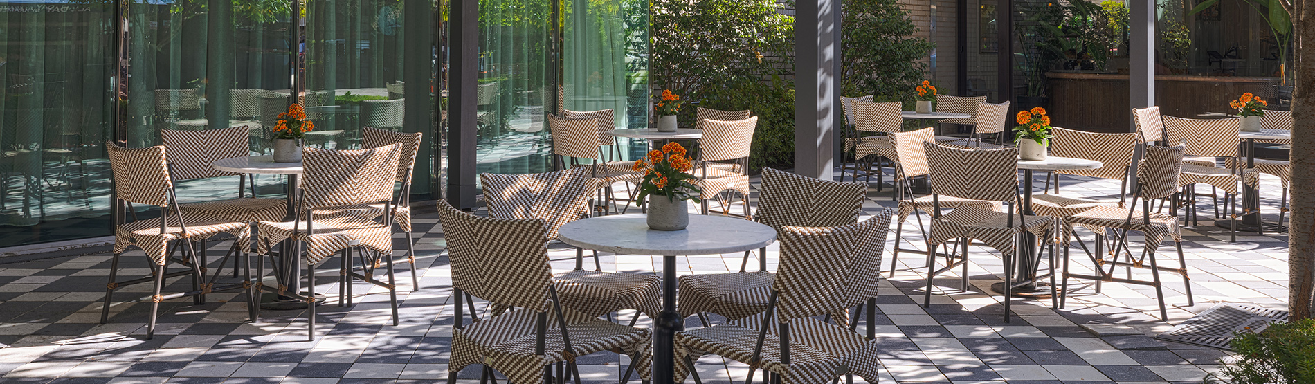 An elevated outdoor view of the Glover Park Terrace, featuring stylish tables and chairs set against a backdrop of lush greenery and urban garden views. The sunlit space offers a peaceful, open-air setting for a social break or private reception.