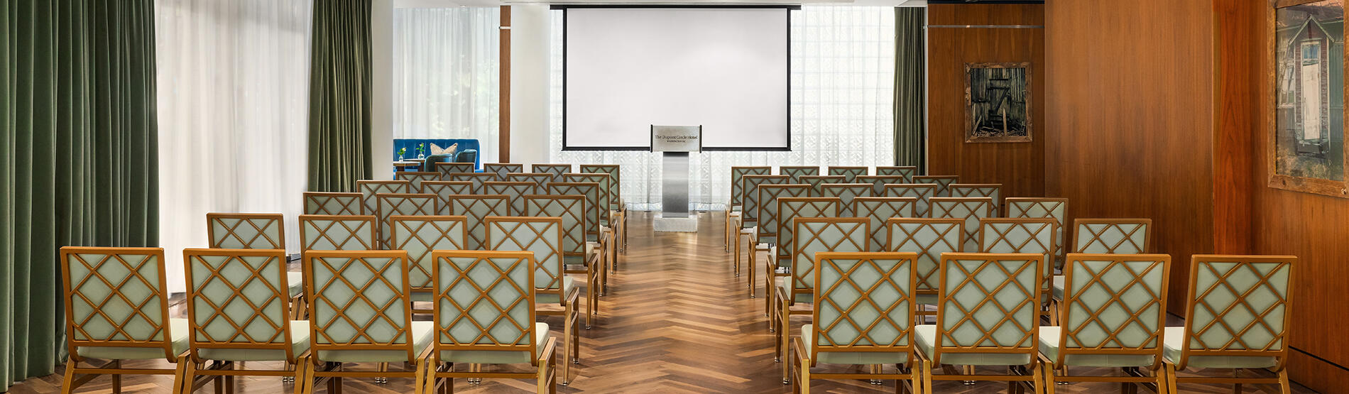 Theatre-style seating arrangement in the Glover Park meeting room, featuring rows of chairs directed toward a speaker podium with large windows in the background.