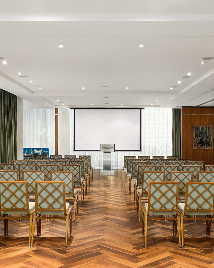 Theatre-style seating arrangement in the Glover Park meeting room, featuring rows of chairs directed toward a speaker podium with large windows in the background.