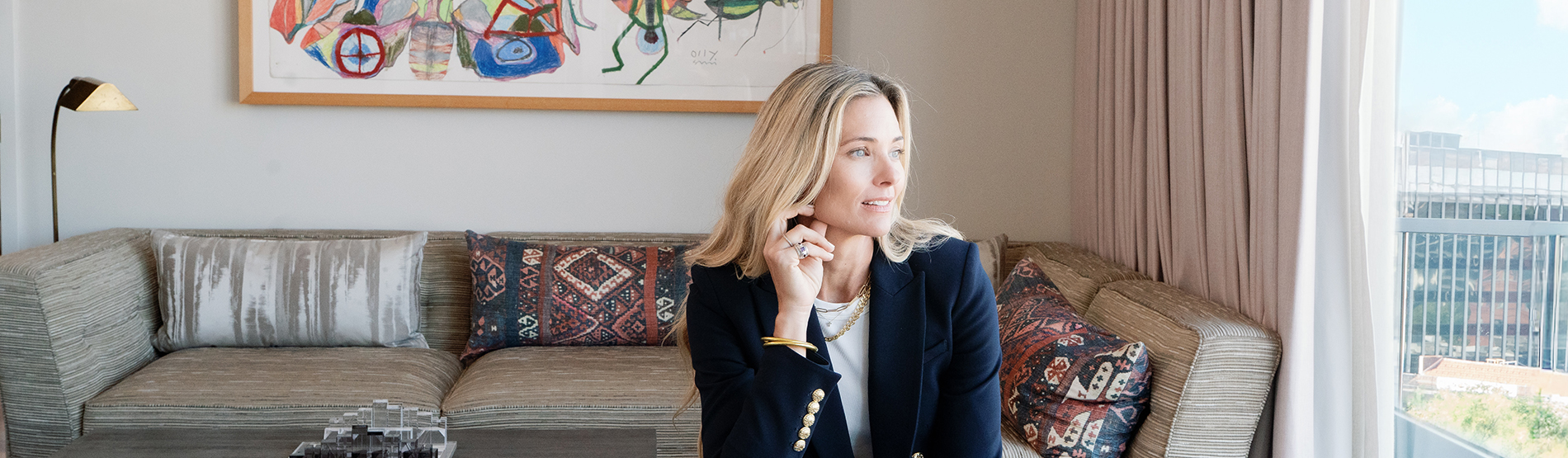 Veronica Beard, dressed in a navy blazer, stands in a suite at The Dupont Circle Hotel, looking out the window as part of "The Blazer Library" offer introduction.